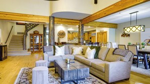 Ein geräumiges Wohnzimmer mit einer großen Couch, einem Couchtisch und einem gemusterten Teppich. Eine Treppe führt auf eine obere Ebene, und im Hintergrund ist eine Küche zu sehen.