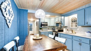 Een keuken met blauwe kastjes, een houten eettafel en een hangende lamp.