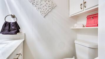 A bathroom with a white vanity, a towel ring, a decorative wall piece, a toilet, and a red storage box labeled "The Beach".