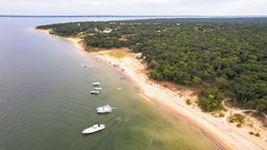 Luchtbeeld van een kustgebied met boten die aan de oever liggen, omringd door dicht bos en een zandstrand.