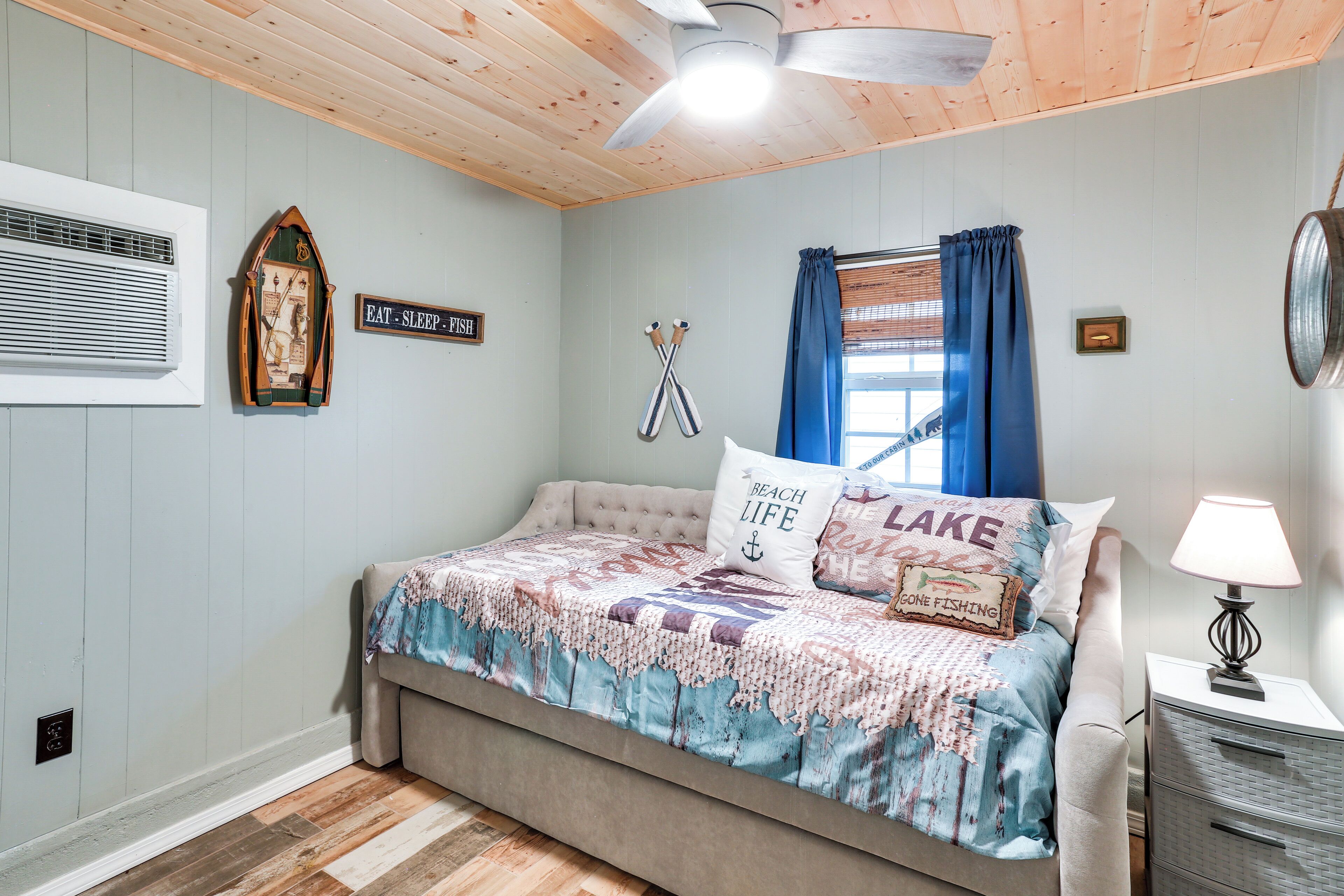A bedroom with a bed, a wall-mounted heater, a sign, a window with curtains, and a lamp.
