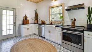 A kitchen with white cabinets, a stainless steel stove, and a window with a view of greenery. - Fire Pit & Yard: Updated Winter Garden Home! (Winter Garden)