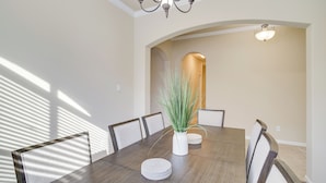 Une salle à manger avec une grande table en bois, six chaises, un vase avec des plantes vertes et un lustre.