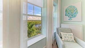 A room with a large window overlooking a natural landscape, a bed with a pillow that says "LOW DOWN WE'RE ON BEACH TIME", and a wall-mounted artwork of a leaf. - Serenity on the Sound, steps to pool/grills (Bradenton)
