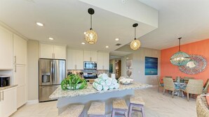 A modern kitchen with a central island, stainless steel appliances, and a dining area with wicker chairs. - Serenity on the Sound, steps to pool/grills (Bradenton)