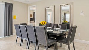 Un comedor con una mesa de vidrio, cuatro sillas tapizadas y un jarrón con girasoles.