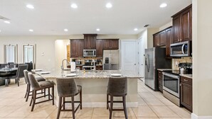 Una cocina amplia con una isla central, armarios de madera oscura, electrodomésticos de acero inoxidable y un comedor con taburetes de bar.