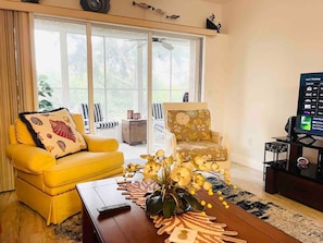 Una sala de estar con un sofá amarillo, un sillón floral y una mesa de centro con un jarrón.