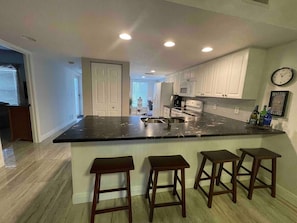 Una cocina moderna con una isla central, taburetes de bar, armarios blancos y un reloj en la pared.