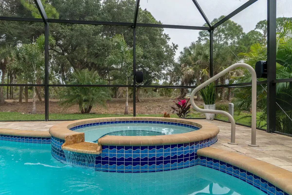 Piscina interior con borde de azulejos, rodeada por un recinto de vidrio y vista a árboles fuera.