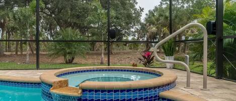 Piscina interior con borde de azulejos, rodeada por un recinto de vidrio y vista a árboles fuera.