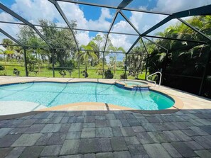 A swimming pool with a metal roof structure, surrounded by a paved deck and lush greenery.