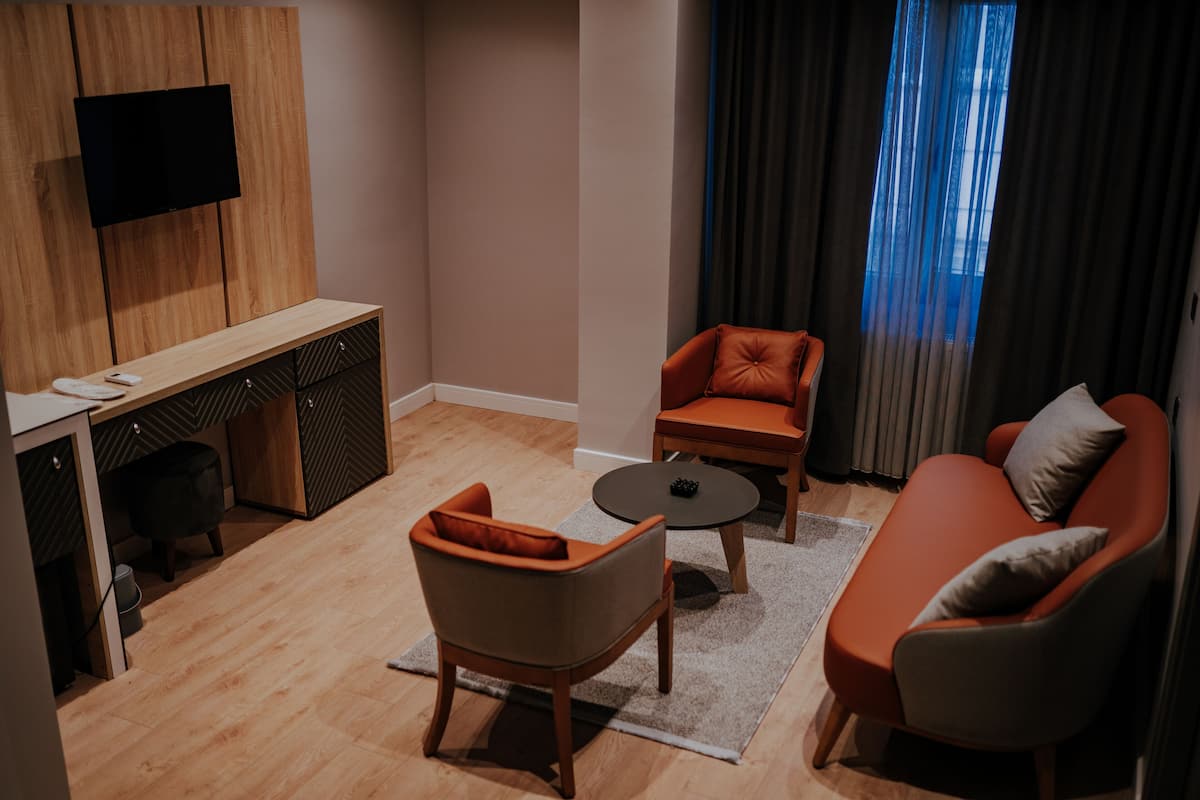 A modern living room with a sofa, armchair, and coffee table. A flat-screen TV is mounted on the wall, and there is a small table with a remote control.