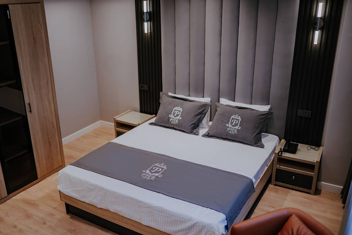 A modern hotel room with a large bed, two bedside tables, a wardrobe, and a brown leather chair.