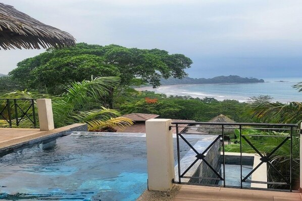 Ein Poolbereich mit Blick auf den Ozean und einer strohgedeckten Struktur.