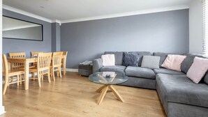 A living room with a grey sofa, a glass coffee table, wooden chairs, and a grey wall. - Chambers Place (No 10) (St Andrews)