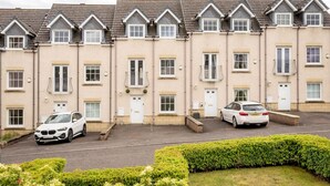 A row of townhouses with a driveway and a white car parked in front. - Chambers Place (No 10) (St Andrews)