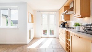 A modern kitchen with wooden cabinets, a gas stove, and a view through a glass door to an outdoor area. - Chambers Place (No 10) (St Andrews)