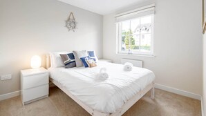 A bedroom with a bed, bedside table, lamp, window, and a wall decoration. - Chambers Place (No 10) (St Andrews)