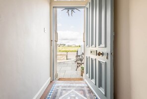 A hallway leading to a door with a view of a garden and a clear sky. - Inglisfield | Earlsferry (Elie)