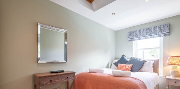 Ein Schlafzimmer mit Bett, Nachttisch, Lampe und einem großen Spiegel an der Wand.