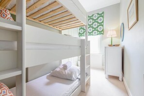 Ein Schlafraum mit Etagenbetten, Holzbalkendecke, einem kleinen Nachttisch mit Lampe und Wandbehang mit Muster.