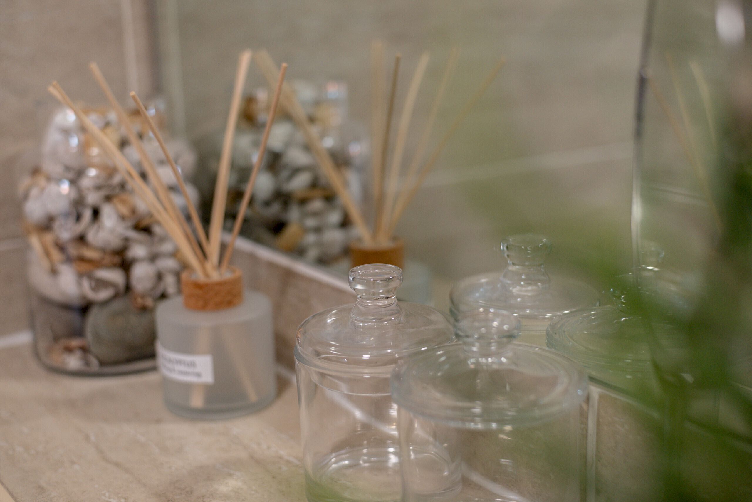 A bathroom with clear glass jars containing reed diffusers and a small bottle of liquid soap.