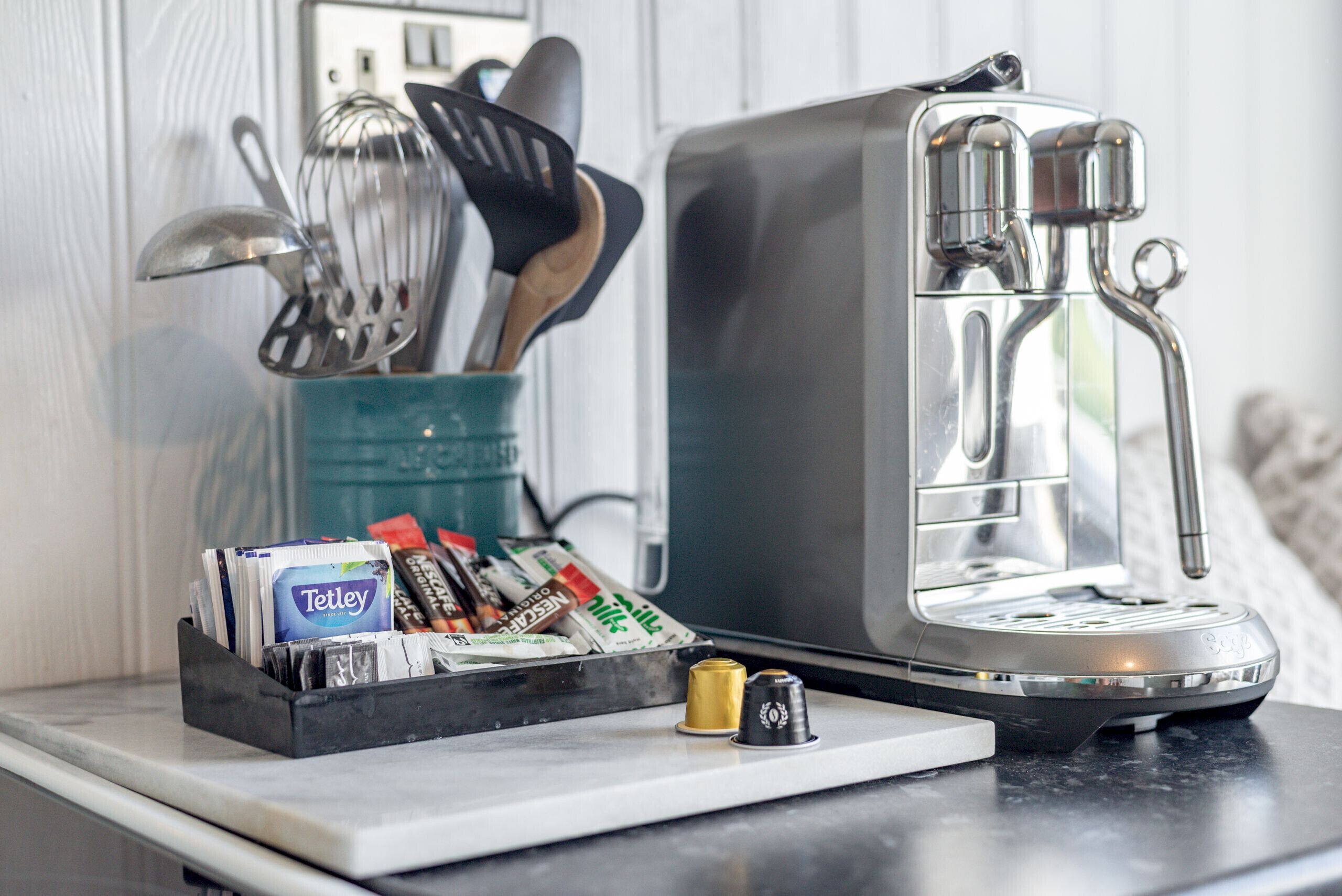 A coffee maker on a kitchen counter with a coffee pod holder and utensils.