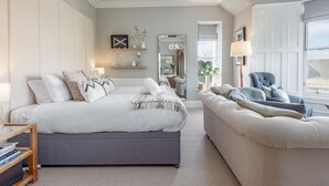 Une chambre à coucher comprenant un lit, un canapé, un miroir, des étagères ornées d’objets décoratifs et une fenêtre donnant sur un paysage agréable.