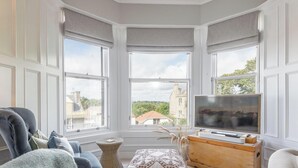 Une chambre d’angle avec de grandes fenêtres, un téléviseur à écran plat, un canapé et un petit meuble en bois.