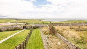 A coastal landscape with a stone wall, grassy fields, and a road leading to a beach.