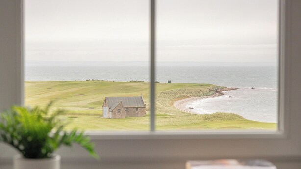 A view of a coastal landscape with a grassy field, a small building, and the sea.