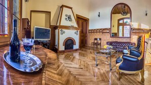 Un salon spacieux doté d’une cheminée, de parquet, d’un canapé et d’un coin repas avec un plateau.