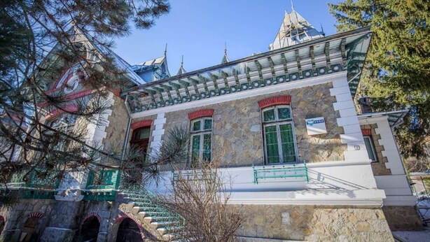 Un bâtiment historique aux murs de pierre, aux encadrements de fenêtres verts et doté d’un toit traditionnel.