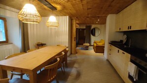 A wooden dining table with chairs, a kitchen area with cabinets, and a yellow sofa in a cozy interior. - Ferme Ancienne 1876 Rénovée, Appartement Neuf Tout Confort 8 Personnes (Le Grand-Bornand)
