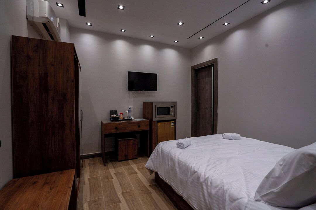Habitación de hotel con cama, televisor montado en la pared, microondas y armario de madera.