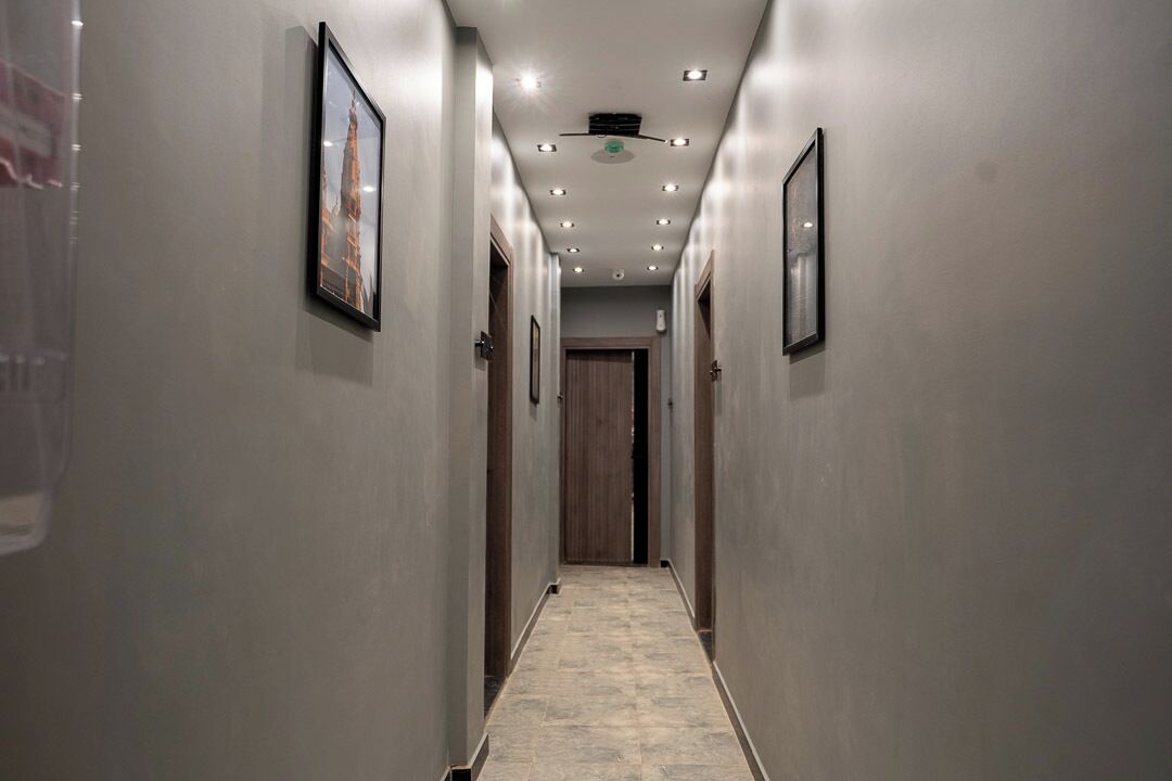A hallway with framed pictures on the walls, recessed lighting, and a wooden door at the end.