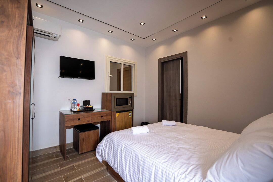 Quarto de hotel com cama, escrivaninha com micro-ondas, televisão e guarda-roupa.