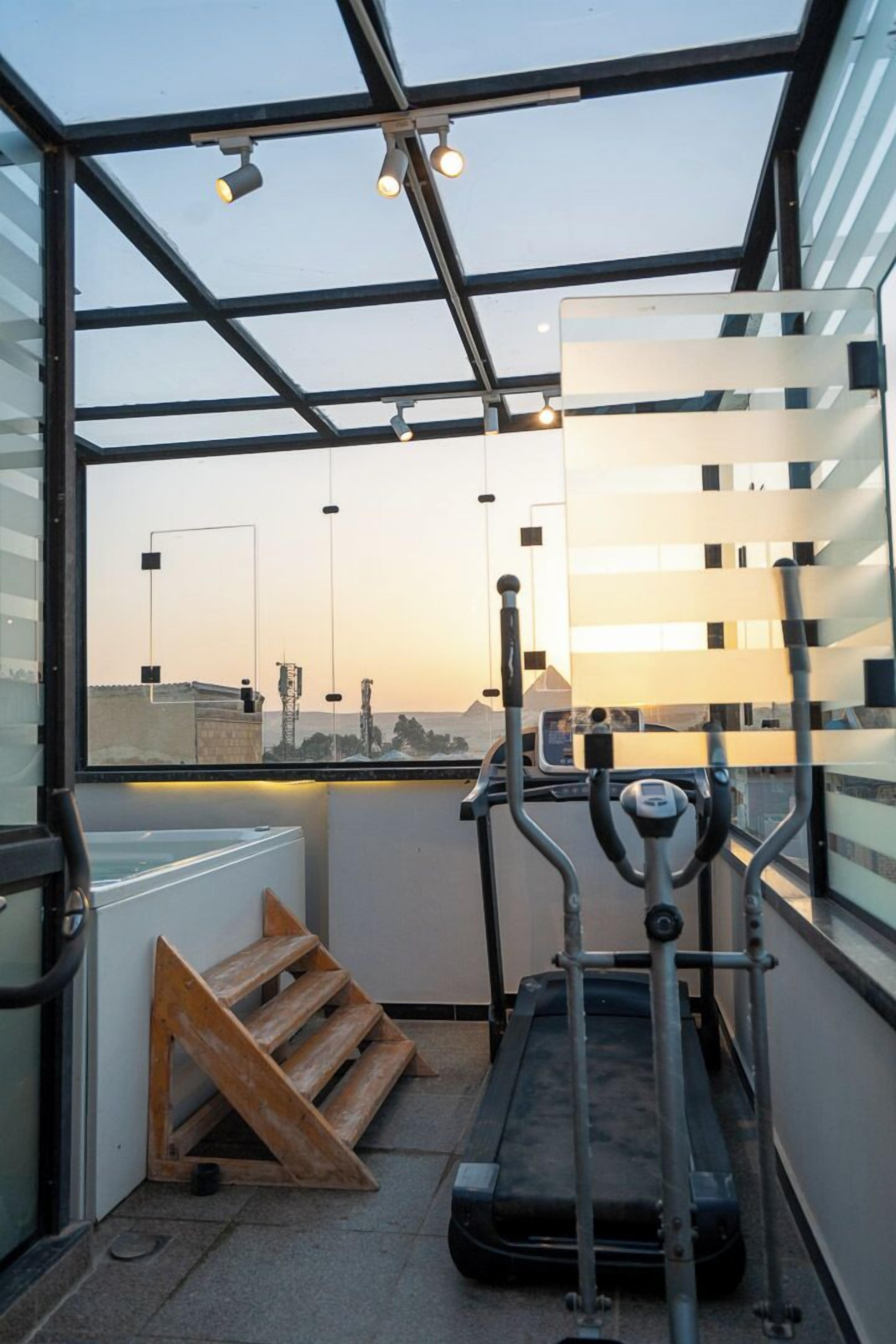 Un gimnasio con cinta de correr, pesas y una ventana con vista a un paisaje urbano.