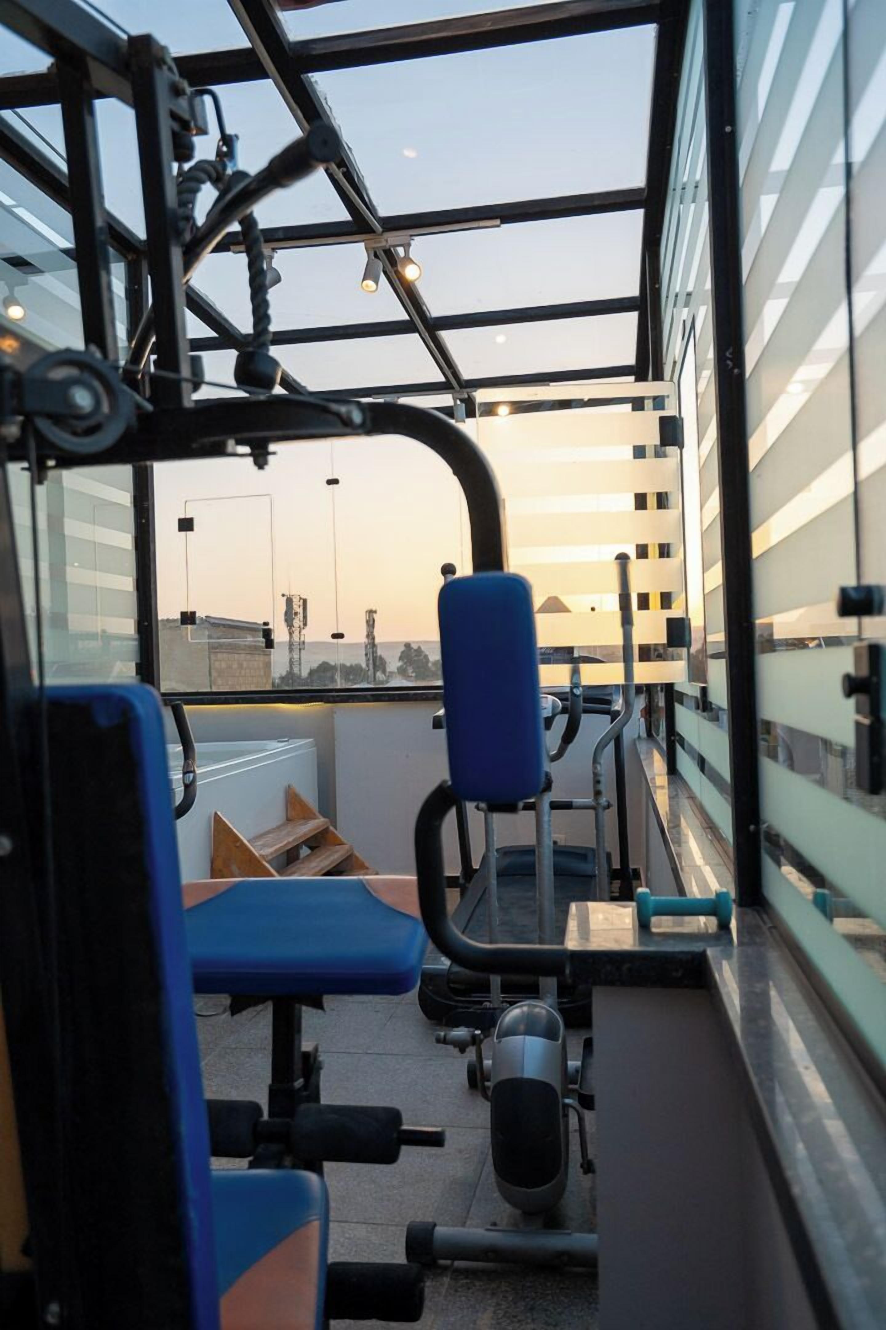 Un gimnasio con equipamiento de ejercicio y vistas a la ciudad a través de amplias ventanas.