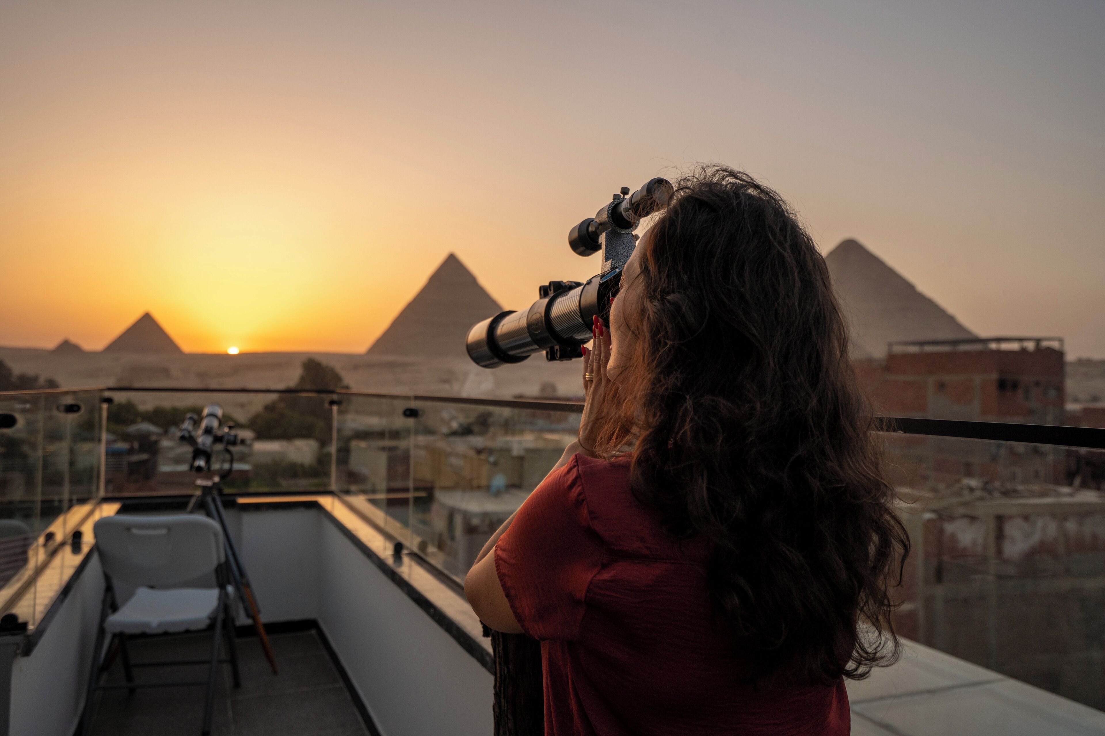 Una persona con una cámara en un balcón, con vistas a las pirámides al atardecer.