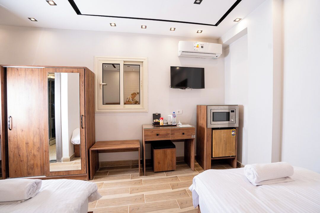 Une chambre d’hôtel avec deux lits, un bureau en bois, une télévision et un appareil de climatisation.