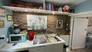 Una cocina compacta con pared de piedra, un lavamanos, un microondas y un escurreplatos.