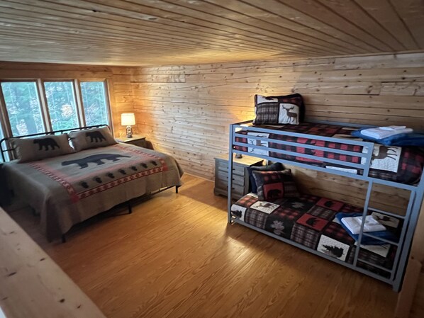 A wooden cabin bedroom with a bunk bed, a desk, and a nightstand with a lamp.