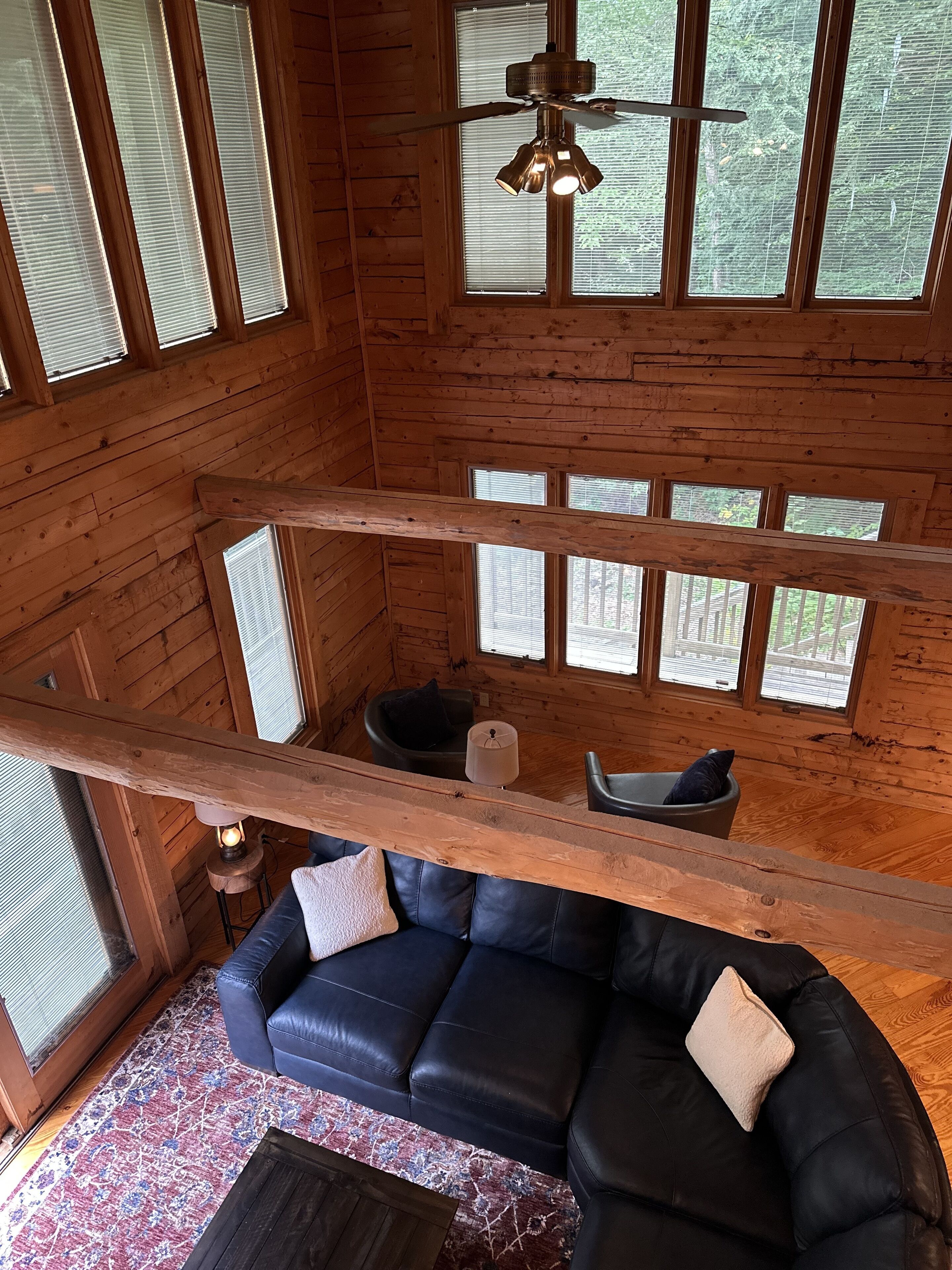 A wooden cabin interior with a black leather sofa, a small table, and a ceiling fan.