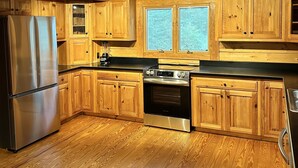 Interno di una baita in legno con cucina, caratterizzata da mobili in legno, un frigorifero in acciaio inox, un fornello e una finestra con persiane.