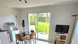 En moderne stue med en lilla sofa, et spiseområde med stole, et køkken og et stort fjernsyn.