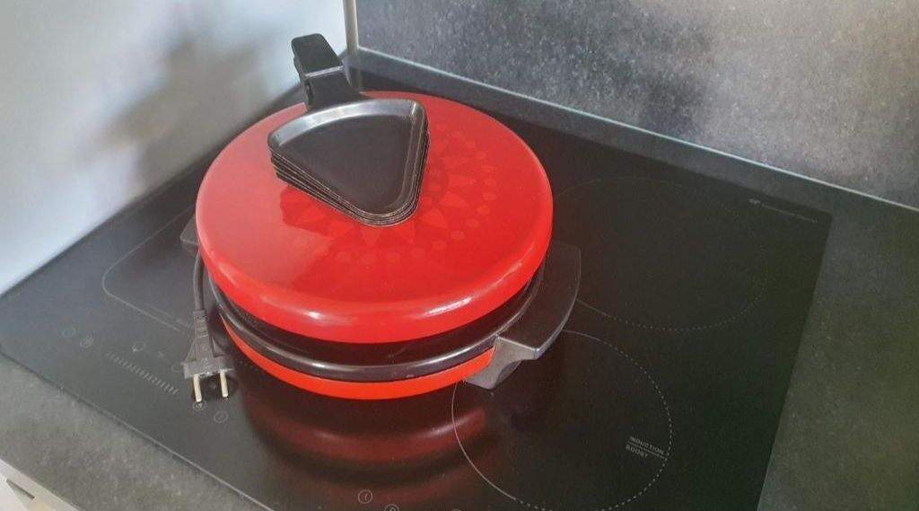 Una fogaira d'inducció vermella amb un panell de control negre i una olla negra a sobre.