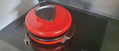 A red induction cooktop with a black control panel and a black pot on it.