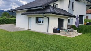 Et moderne hus i to etager med velholdt græsplæne, terrasse med udendørs møbler og garage.